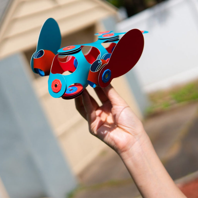 a child holds up their red and blue areoplane made from clixo pieces
