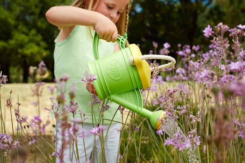 a child watering wildflowers with her green toys watering can