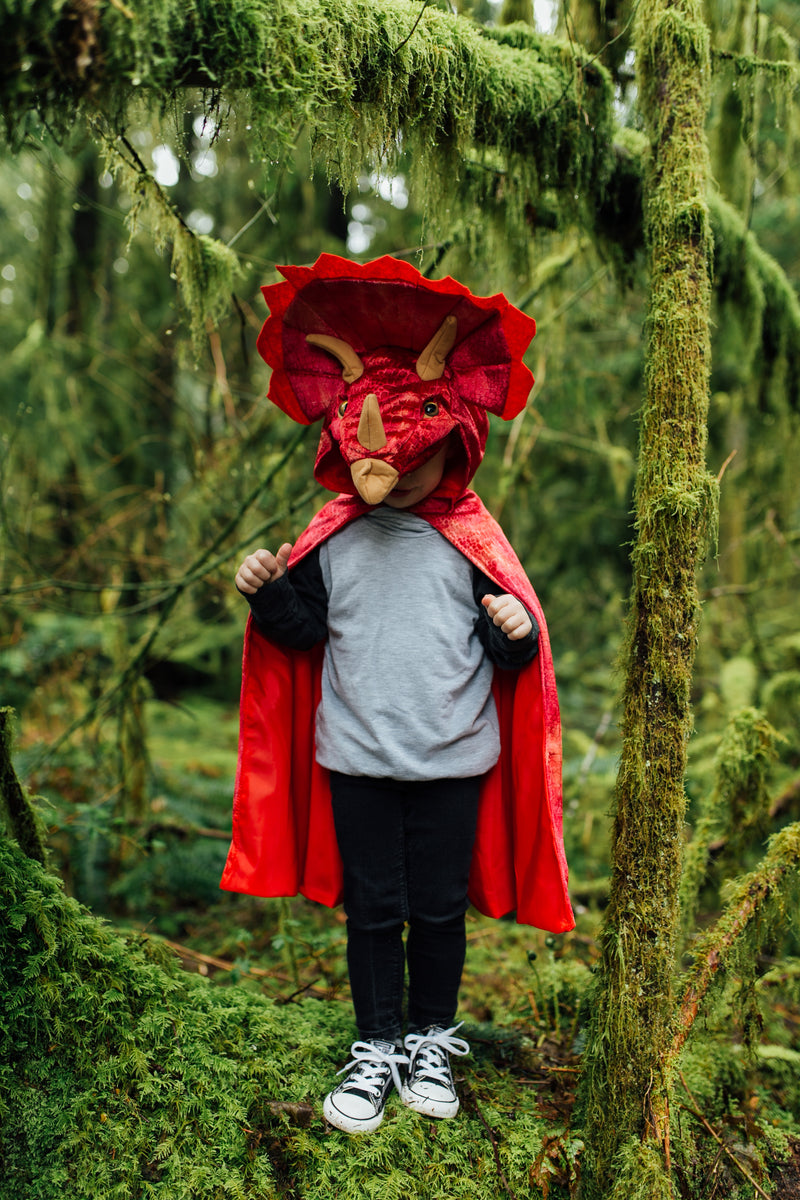 a kid runs through the jungle in his red triceratops dinosaur costume by great pretenders