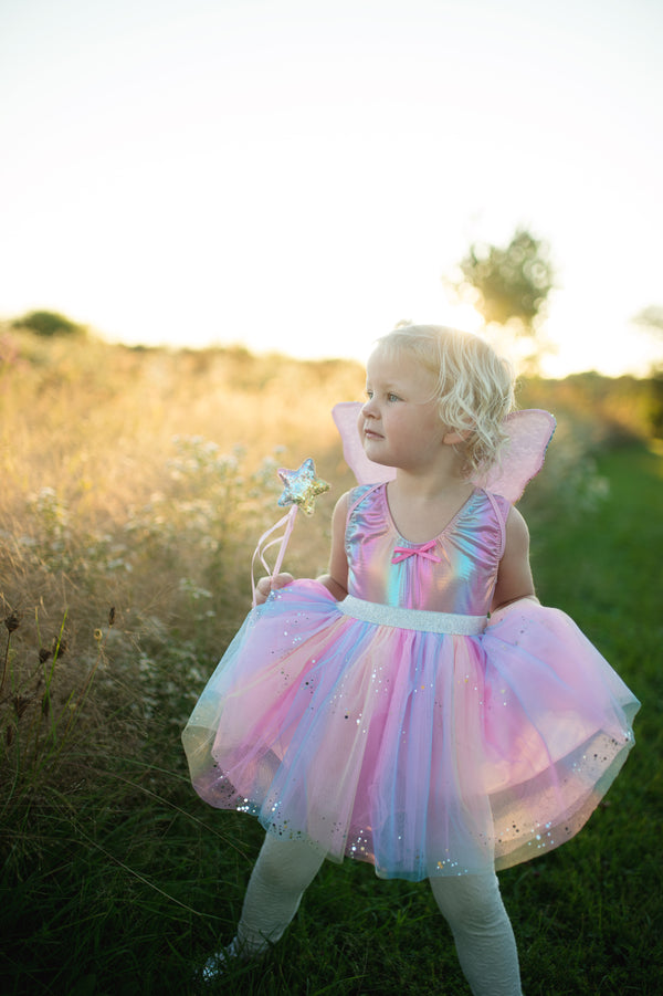 girl stands in a field with her rainbow fairy costume with wings on and her sequin wand