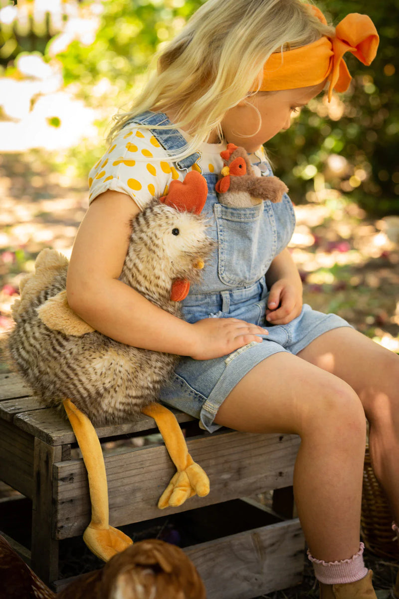 a girl holds her rooster soft toy under her arm sitting outside in the autumn