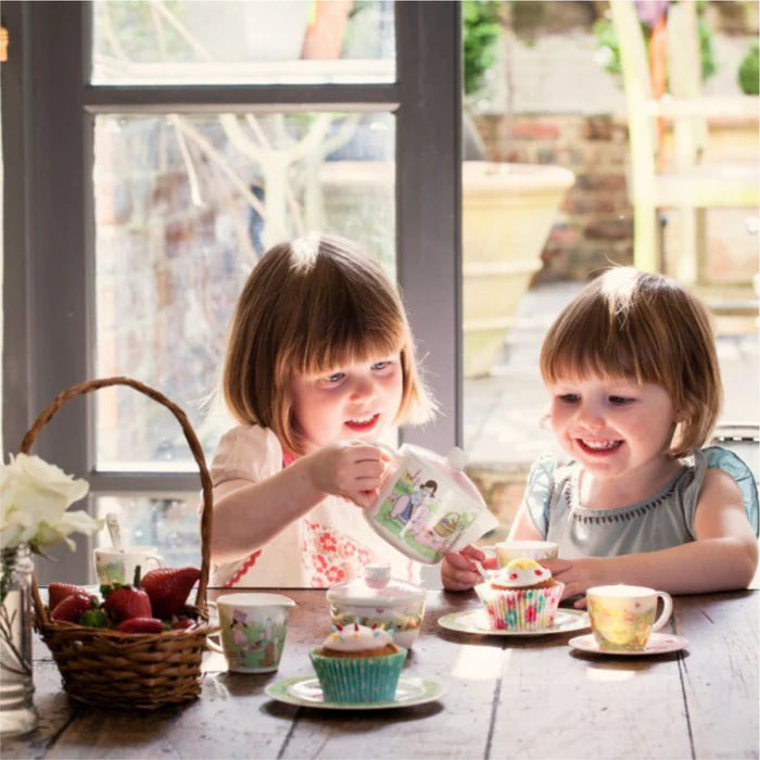 Two young girls enjoying a tea party with cupcakes and tea cups at a table by a window.