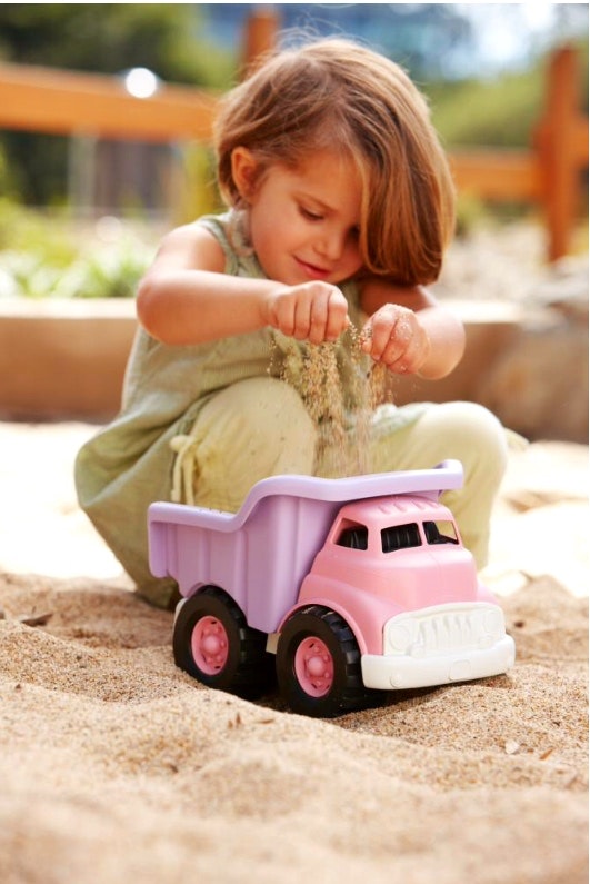 a child plays with a green toys dump truck in purple and pink in the sand pit