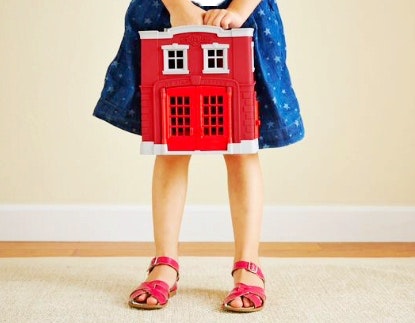 a girl in a blue dress holds her green toys red fire station 