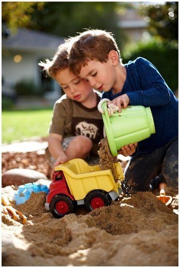 two kids play in the sand pit with their green toys sand bucket and truck