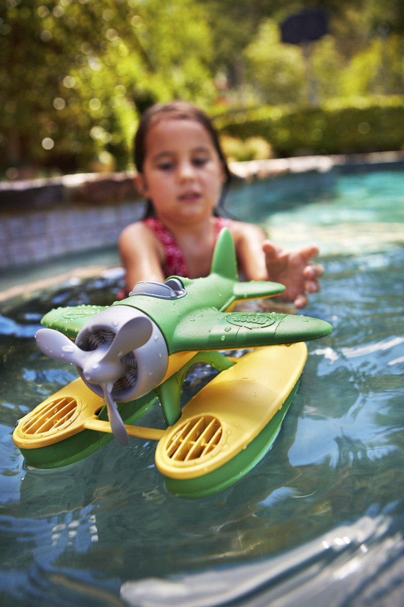 a girl pushes her green toys sea plane in the pool