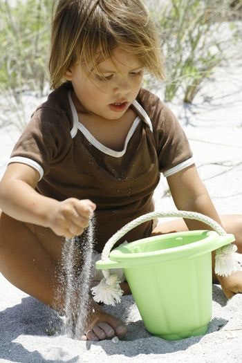 a child puts sand into his green toys sand bucket at the beach