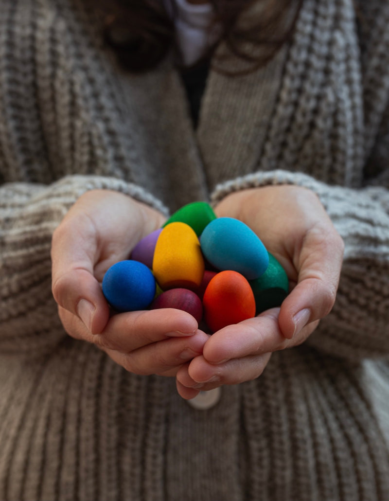 a child holds a selection of rainbow wooden mandala rainbow eggs in their hands