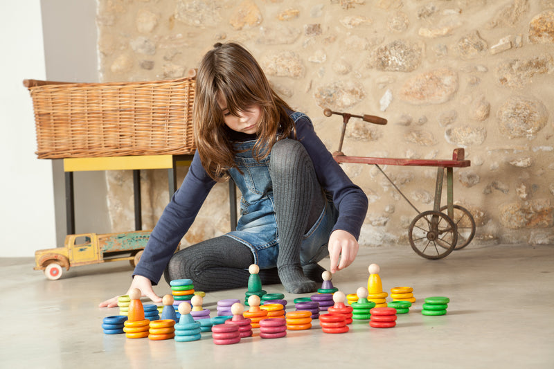 A wonderful image of open-ended play with the Grapat nins carla pieces including rainbow coloured wooden people, rings and coins.