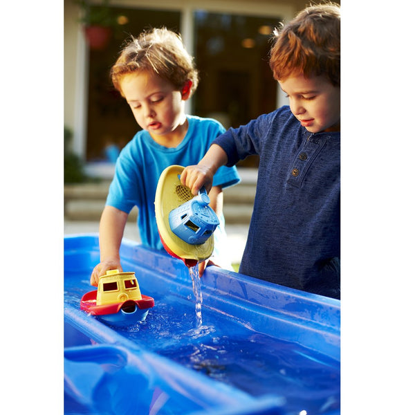 two kids play with a water trough and their green toys tug boats