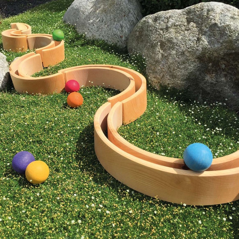 the pieces of the grimms large rainbow have been put together outside to create a long snake shape for balls to run along
