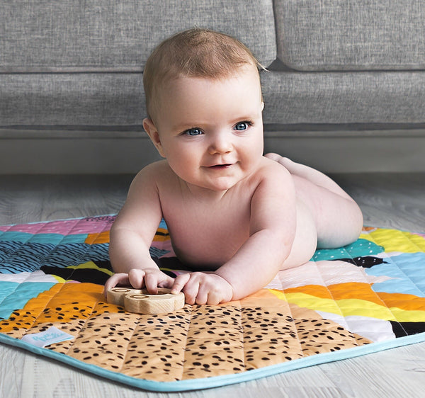 a baby lays out on the rudie nudie printed waterproof play mat