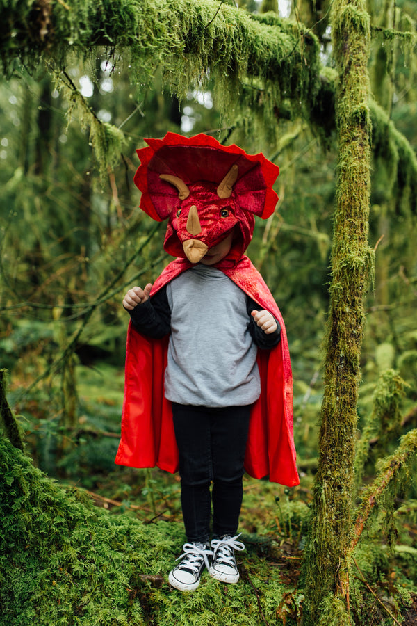 a kid runs through the jungle in his red triceratops dinosaur costume by great pretenders