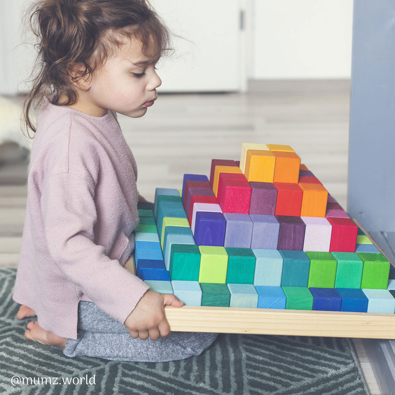 a child plays with the grimms large step pyramid in rainbow coloured blocks