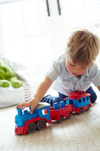 a child pushes the green toys train set along the carpet inside