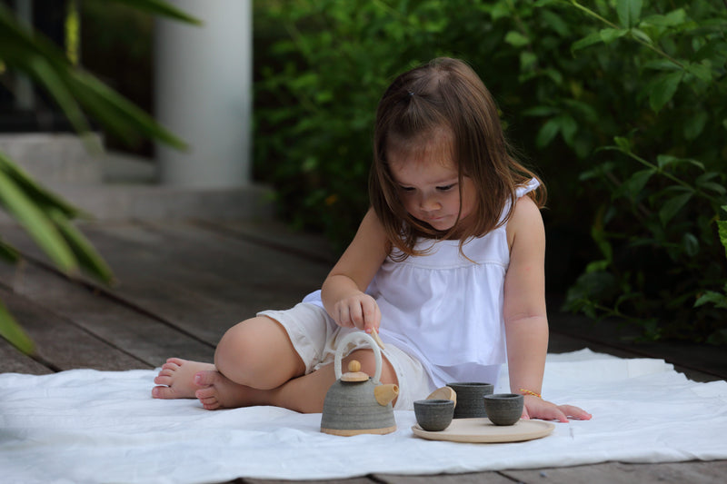 a child sits with her plan toys wooden tea set