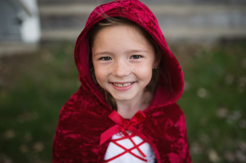 a girl wears a red hooded cape by great pretenders kids costumes
