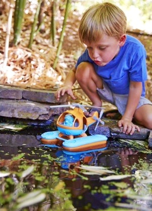 a child puts his green toys helicopter in the pond to float