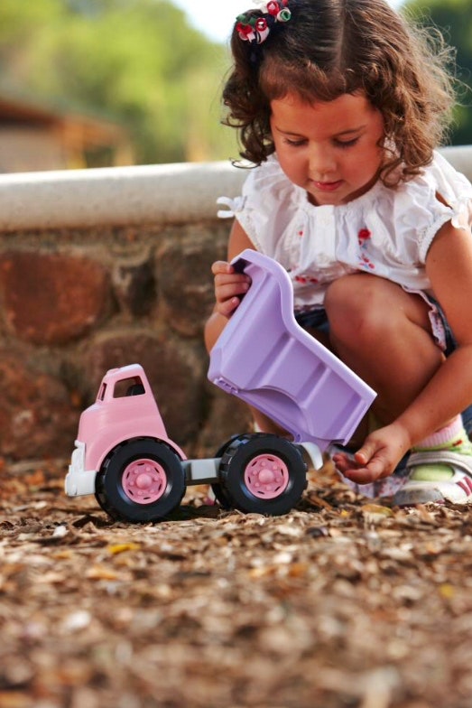 a girl lifts up the tray of her green toys purple dump truck