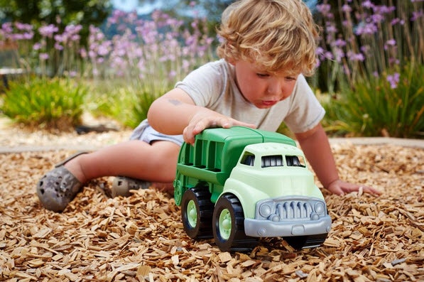 a child pushed the green toys recycling truck through the tan bark